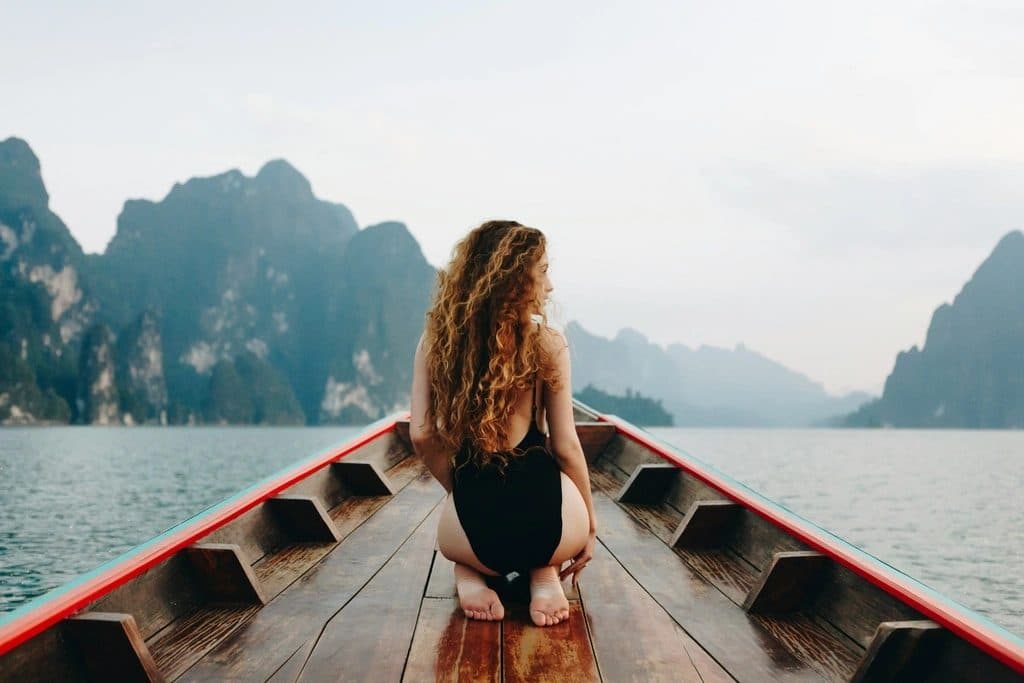 A woman sitting at the bow of a longtail boat on a lake between limestone cliffs, the featured image of the post